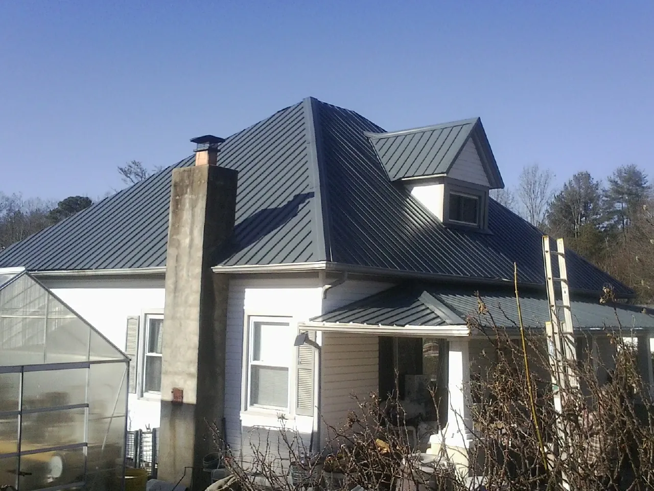 Dark blue standing seam metal roof on a white farmhouse with dormer — Slate & Tile Roof Repair by Roofing Brothers in Holbrook
